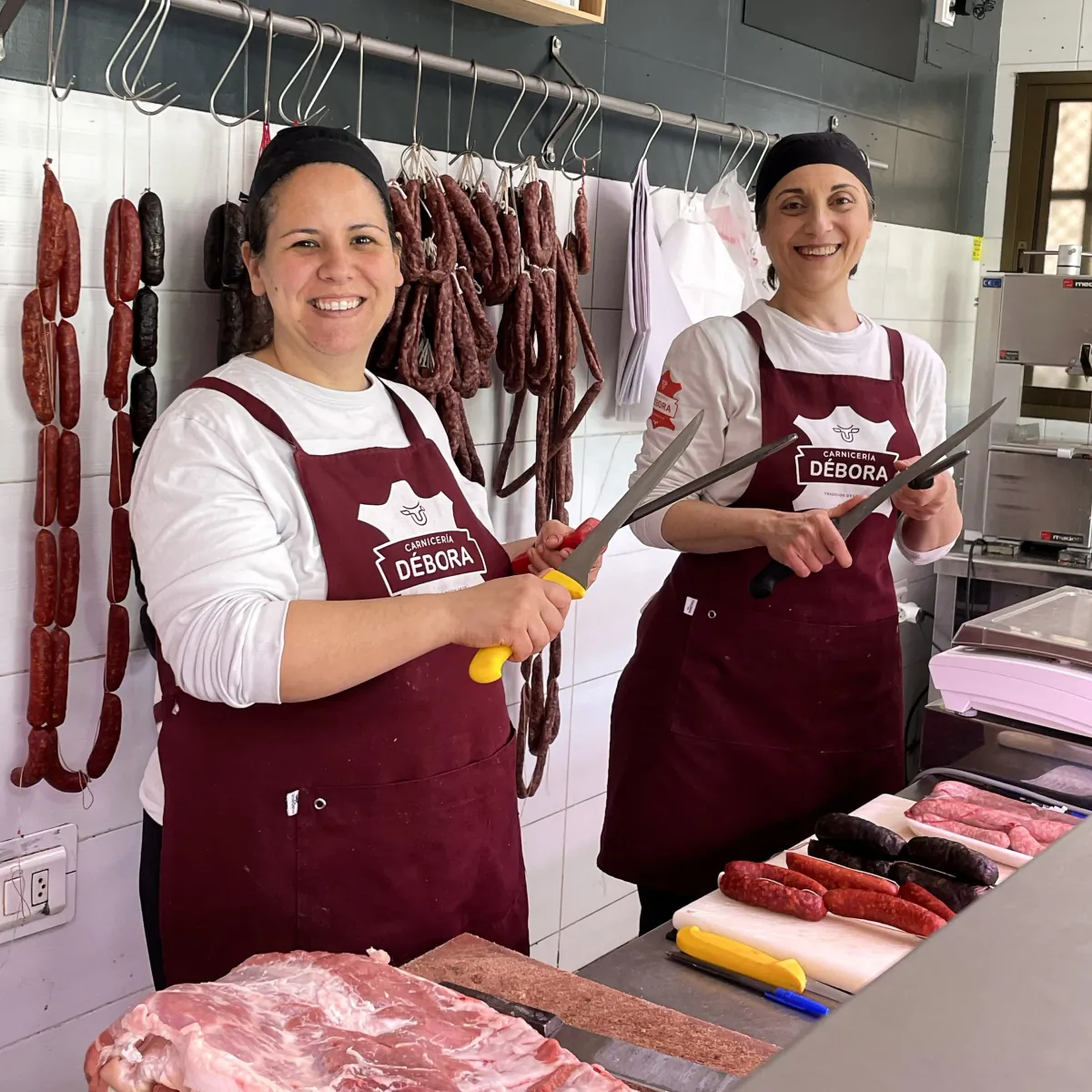 Dos carniceras de Carnicería Débora sonriendo en la tienda, rodeadas de embutidos caseros